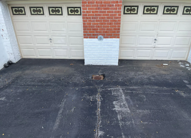 Two white garage doors with a brick and painted wall, on a black asphalt driveway.