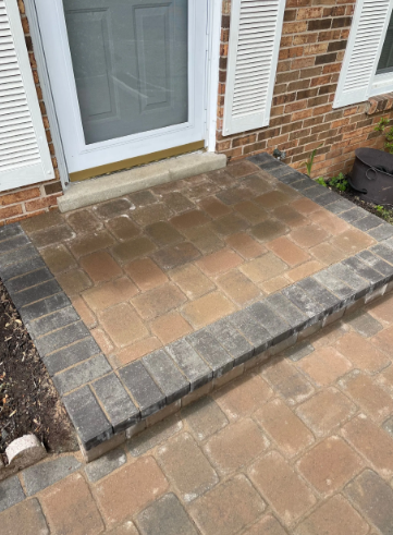 Brick patio leading to a white door, bordered by gray bricks, set against a brick building.