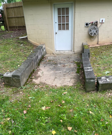 Concrete ramp leading to white door in a tan brick building. Green grass surrounds it.