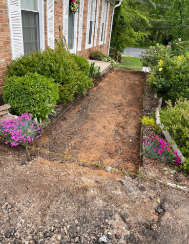 Garden bed prepared for planting, bordered by wood and established plants near a brick house.