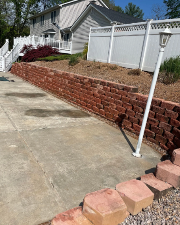 Brick retaining wall along a driveway next to a white fence and a house.