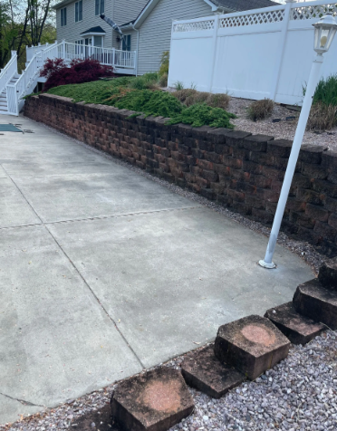 Concrete driveway bordered by a dark brick wall with greenery above.