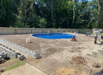 Construction of a pool area in a backyard. Workers, cinder blocks, gravel, and a blue pool in progress.