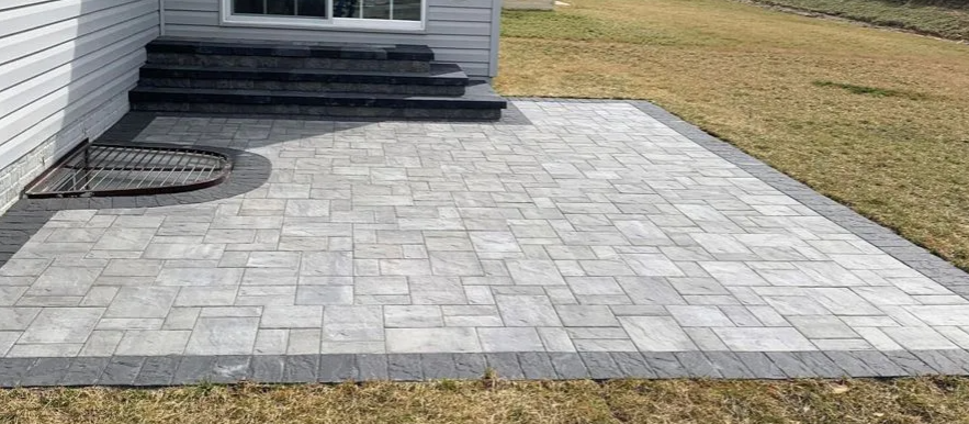 Patio with gray pavers, dark gray border, steps, and house siding.