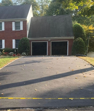Asphalt driveway in front of a brick house with a two-car garage. Yellow caution tape is visible.