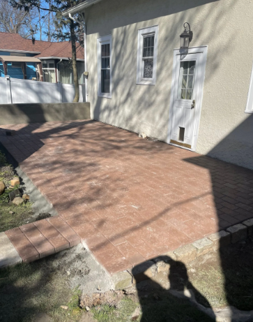 Brick patio next to a house with a white door, windows, and a black light fixture.