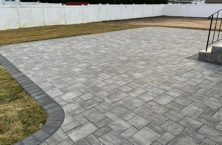 Overhead view of a swimming pool with gray brick patio. A person stands on the steps near the house.