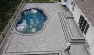 Overhead view of a gray paver patio with a pool. A worker stands nearby.