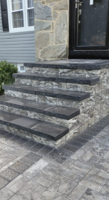Stone steps leading up to a front door with a stone facade, gray pavers on the ground.