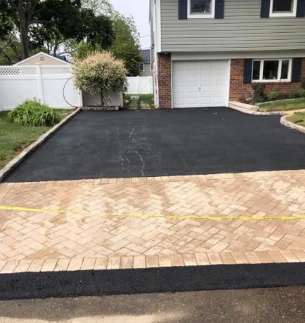 Driveway paved with black asphalt and brick edging leading to a house with a garage.