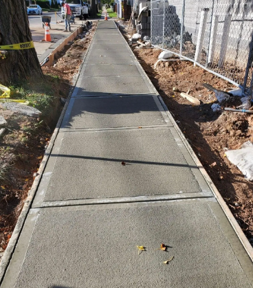 Newly poured concrete sidewalk with wooden forms and adjacent construction.