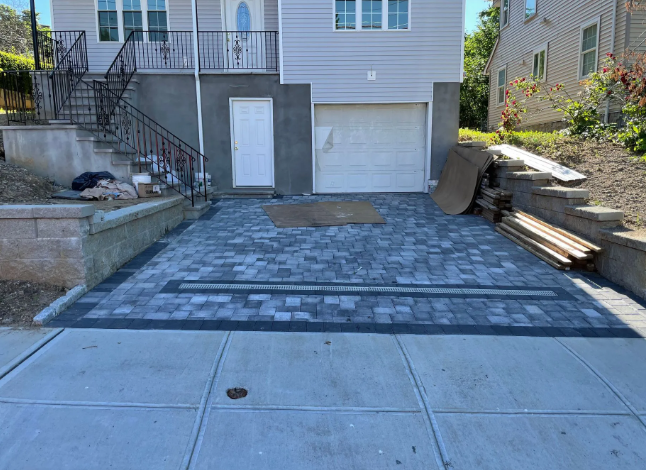 Paver driveway in front of a house, with garage door and steps to the entrance.