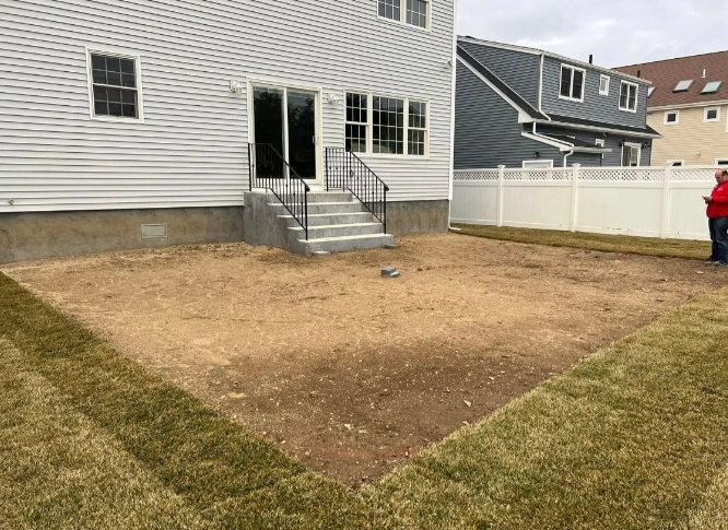 Backyard with bare dirt area, steps to house, grass border, white fence.