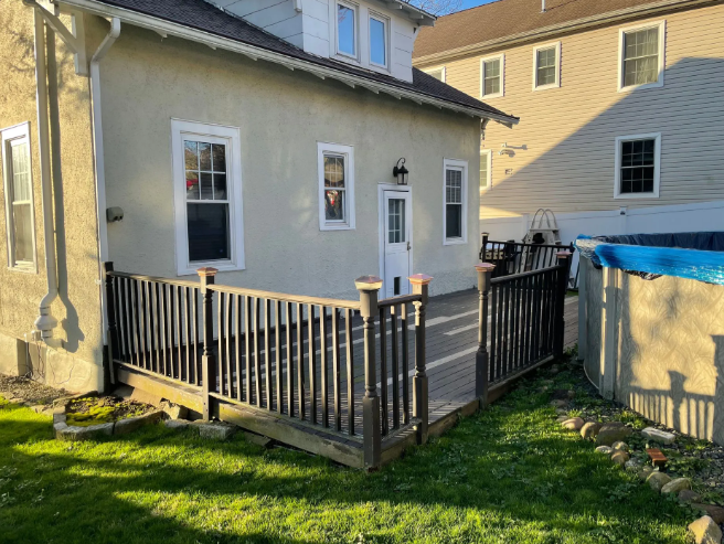 Backyard deck attached to a light-colored house; wooden railings and green grass.