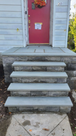 Exterior view of a house's entrance with four stone steps leading to a red door.