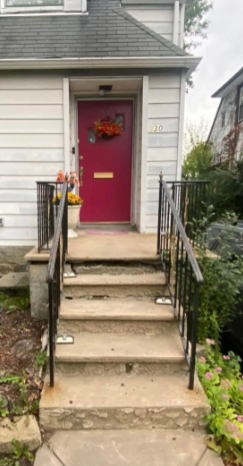 Concrete steps leading to a magenta door with a wreath on a house with a white exterior.