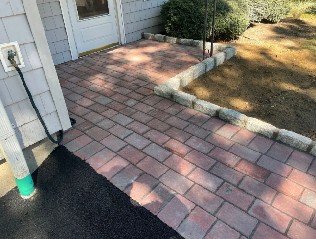Brick pathway leading to a front door with a small, neatly edged flower bed.