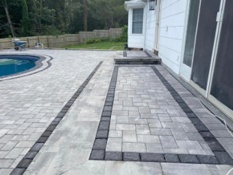 Paver patio with a pool and house entrance; gray and black brickwork.
