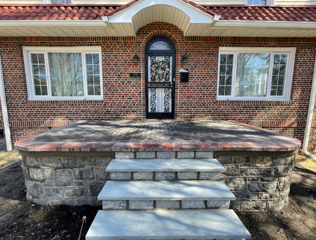 Brick house facade with stone steps leading to the front door; arched entry with metal security door.