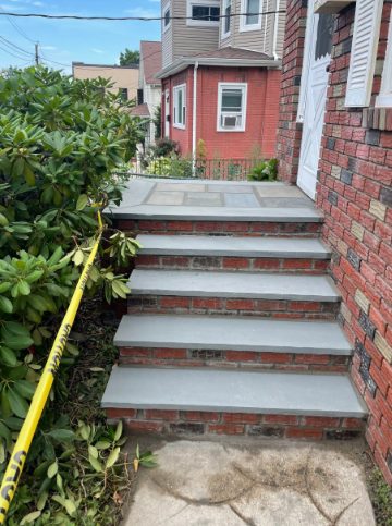 Brick steps with gray stone treads leading to a red brick and white-doored house. Yellow caution tape.
