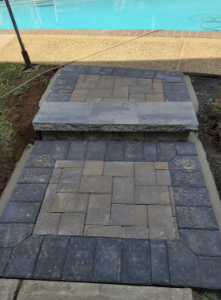 Two-step brick pathway leading to a pool. Gray and brown bricks are arranged in a step formation.