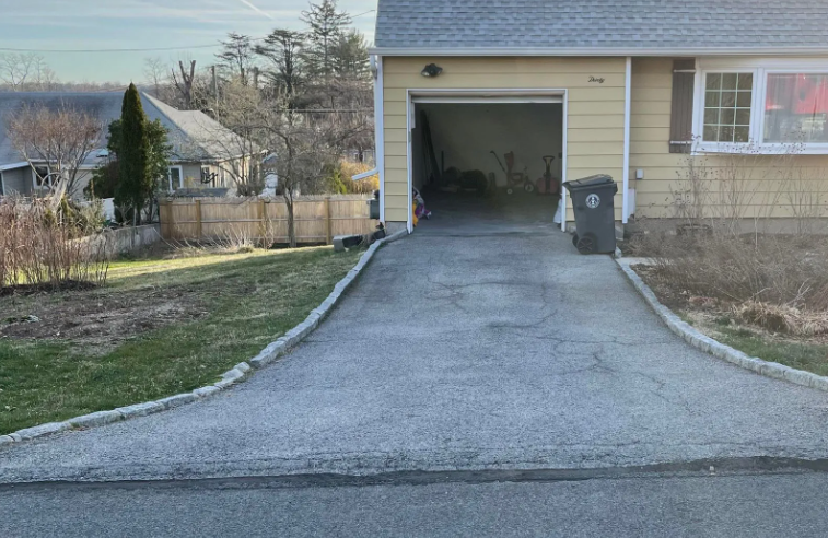 Asphalt driveway leads to open garage. Light yellow house with green lawn on either side.