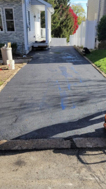 Newly paved asphalt driveway leading to a white house with an open entrance. Blue markings visible.