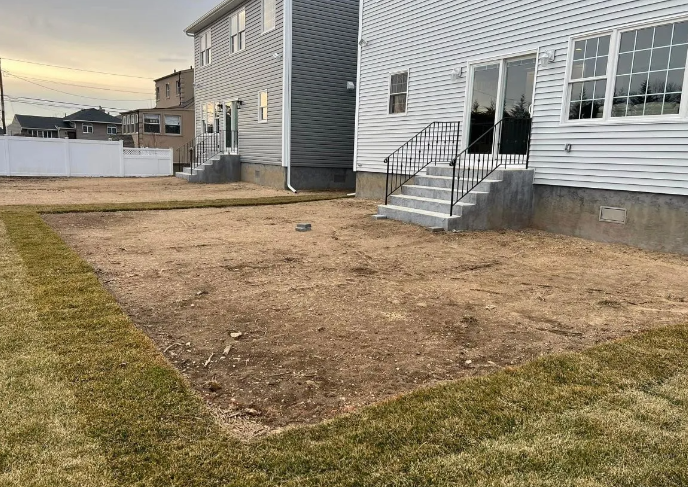 Backyard of two-story houses; dead grass patch surrounded by green lawn; concrete steps and sliding glass doors.