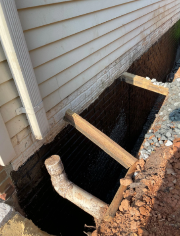 Foundation repair. Black waterproofing covers brick foundation. Wooden bracing and trench visible.