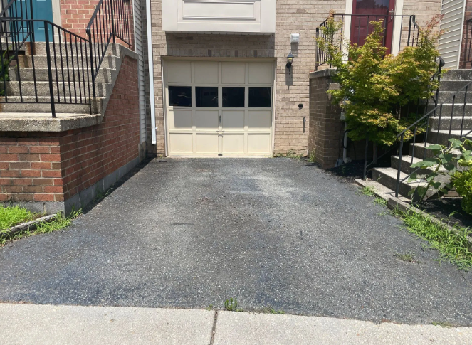Asphalt driveway leading to a garage. Stairs on either side, with a brick and beige facade.