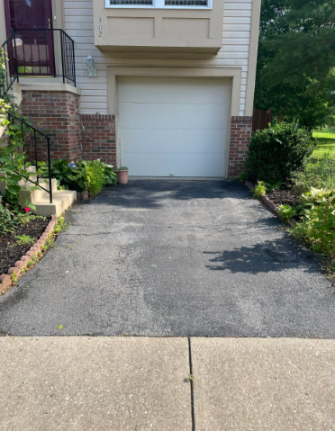 Driveway leading to a garage door, flanked by landscaping and a sidewalk.