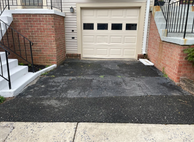 Asphalt driveway in front of a tan garage with brick walls and stairs on either side.