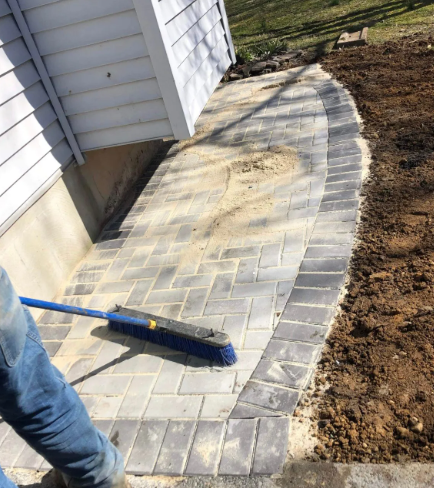 A person sweeping newly laid brick pavers of a curved walkway along a white building.