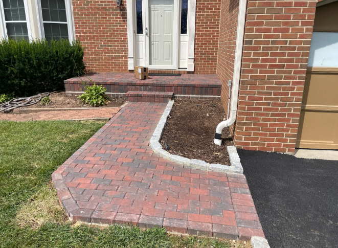 Brick pathway and steps leading to a white door, with a green lawn on the left and a garage on the right.