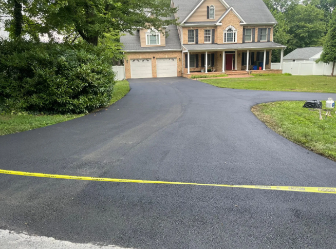 Newly paved asphalt driveway leading to a two-story house with a front porch and garage.