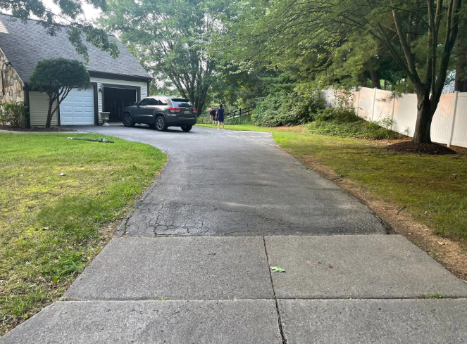Asphalt driveway leading to a garage with a dark gray car. Green lawn on the sides.