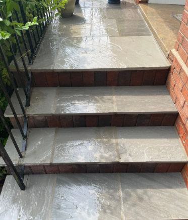 Stone steps with brick risers, wet from rain. Black railing on left, brick wall on right.