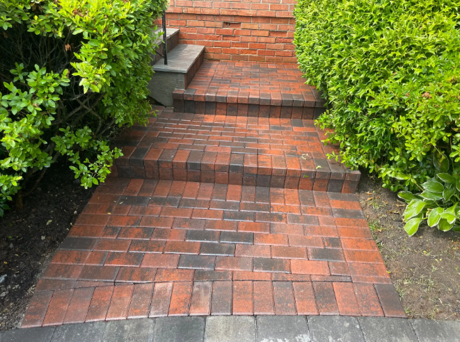 Brick pathway and steps leading up to a building, flanked by green bushes.
