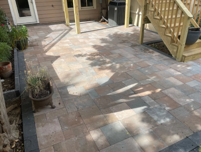Paver patio with a brown and gray color scheme, under a deck and near stairs.