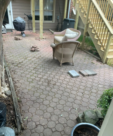 Brick patio with wicker chairs, grill, and wooden stairs.