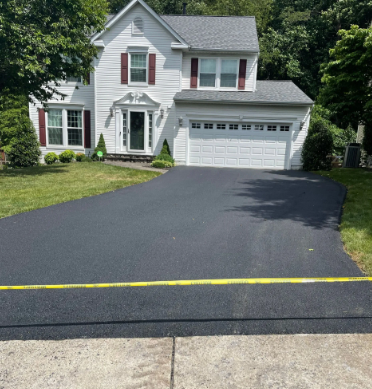 White house with a newly paved black driveway. Red shutters and a green lawn.