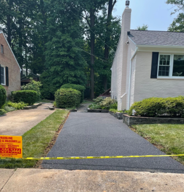 Newly paved asphalt driveway with a yellow caution tape, between lawns and houses.