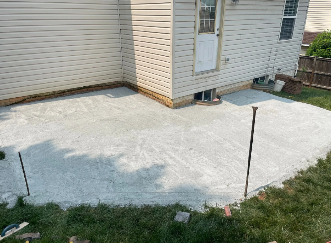 A newly poured concrete patio next to a house with a door, surrounded by grass.