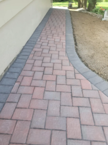 Brick pathway with a dark gray border next to a building and lawn.
