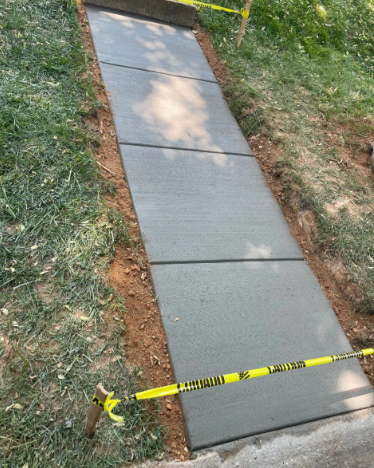 New concrete walkway bordered by grass and dirt, with yellow caution tape.