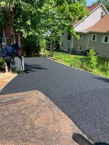 Asphalt driveway being installed; worker applying sealant near a house.