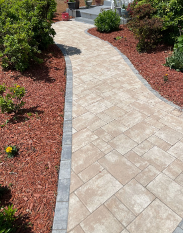Newly paved asphalt driveway with caution tape, leading to a house in a yard with green trees.