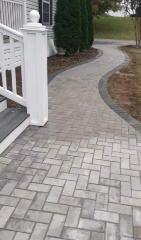 Brick walkway leading from white porch steps to the right, bordered with a darker brick.
