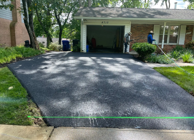 Newly paved asphalt driveway in front of a brick house. Two workers near the garage.