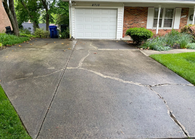 Cracked concrete driveway in front of a house with a closed garage door and green lawn.